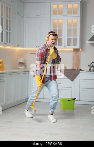 Handsome young man with headphones singing while cleaning kitchen Stock Photo