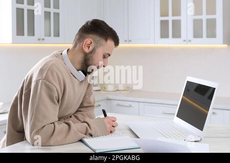 Young man using modern laptop for studying in kitchen. Distance learning Stock Photo