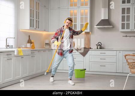 Handsome young man with headphones singing while cleaning kitchen Stock Photo