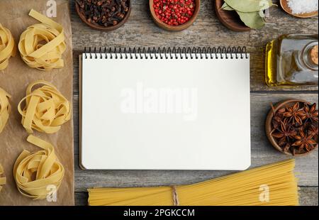 Blank recipe book, spices and raw pasta on wooden table, flat lay. Space for text Stock Photo