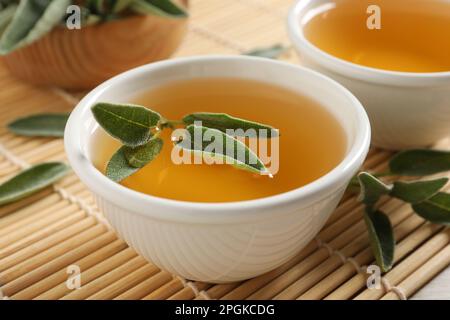 Cup of aromatic sage tea with fresh leaves on table, closeup Stock Photo