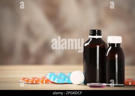 Bottles of syrup, dosing spoon and cough drops on wooden table. Space for text Stock Photo