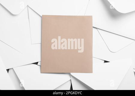 Blank brown card on pile of white paper envelopes, top view Stock Photo