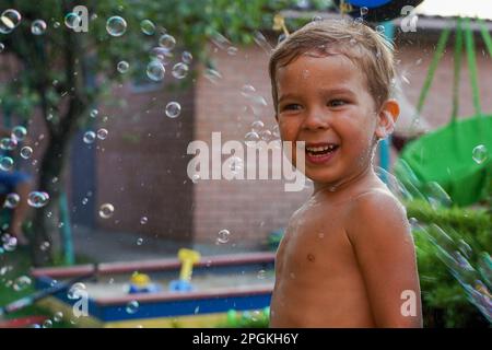 A white boy on the playground in a stream of soap bubbles. Happy summer day. Soft focus Stock Photo