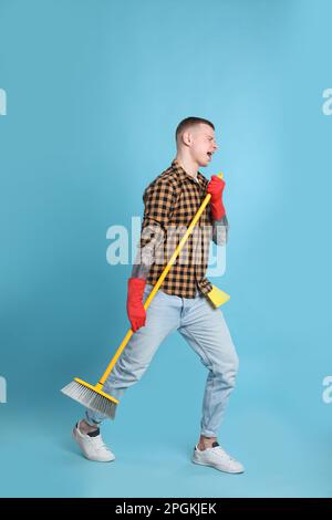 Handsome young man with floor brush singing on light blue background Stock Photo