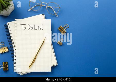 Flat lay composition with unfilled To Do list and glasses on blue background, space for text Stock Photo