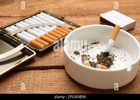Cigarettes in case and ashtray with stubs on wooden table, closeup Stock Photo