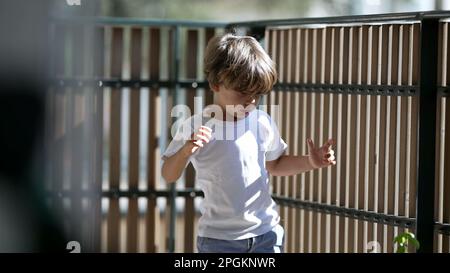 Child holding into balcony wooden fence at apartment residential building. Concept of security and protection of little boy at terrace Stock Photo