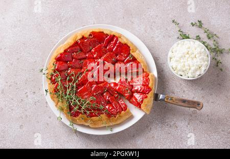Homemade Tarte Tatin with bell red pepper and puff pastry served with thyme and soft cream cheese on a beige textured background, top view Stock Photo