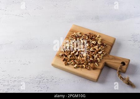 Wooden board with chopped walnuts on light gray background, top view, copy space Stock Photo