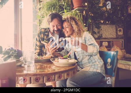 Happy couple of tourist man and woman leaving online review for a cafe restaurant lunch. Happy people enjoying brunch together in a france style coffe Stock Photo