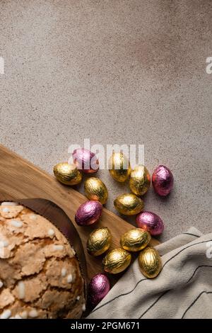 Easter dove cake or bread kulich with chocolate Easter eggs, wooden cutting board, striped napkin on concrete background. Vertical, place for recipe Stock Photo