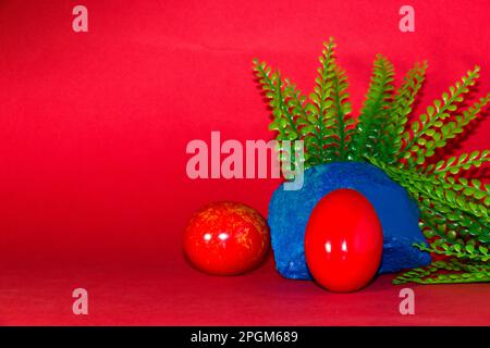 red egg on the blue stone with plant, creative art holiday design on the red background Stock Photo