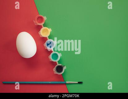 Easter egg with watercolor and paint brush on red and green background. Minimal concept of Easter. Flat lay, top view, copy space. Stock Photo