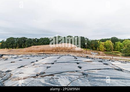 Weighted plastic sheeting covers a hillside in an active landfill.  Probably PVC geomembranes with a tree-line in the distance. Stock Photo