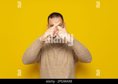 Bearded hispanic man in beige turtleneck shows hands to stop timeout, X fingers. Isolated over yellow background. Stock Photo