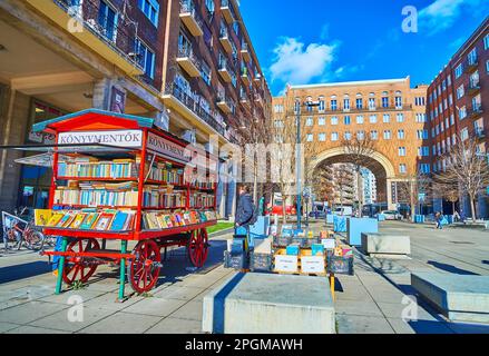 BUDAPEST, HUNGARY - FEB 22, 2022: The vintage style book kiosk on Imre Madach Square with red brick Madach Houses with tall colonnade and arched pass Stock Photo