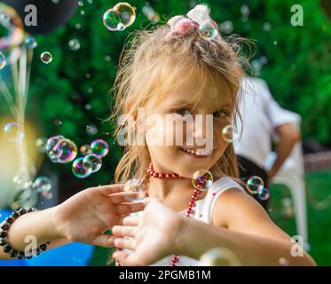 A girl dances in soap bubbles at a children's party. Children's birthday party in the backyard in the summer. Beauty in bubbles Stock Photo