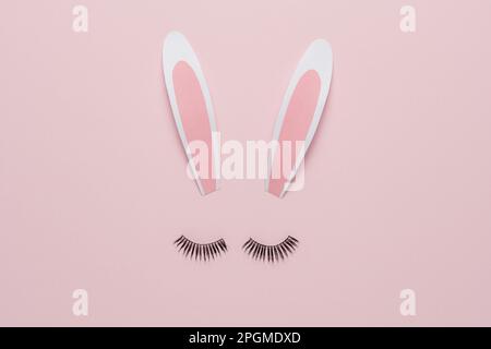Minimal Easter concept. Bunny rabbit face made of paper bunny ears with eyelashes on pastel pink background. Flat lay. Stock Photo