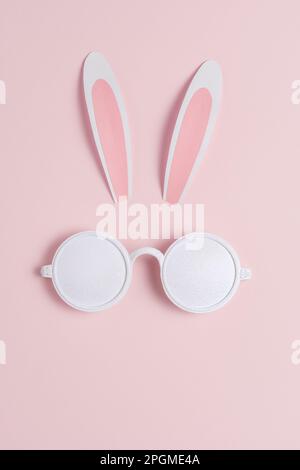 Creative Easter concept with bunny ears and white sunglasses on pink background. Minimal Easter concept. Stock Photo