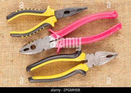 Three pliers combined on a jute cloth, macro, top view. Stock Photo