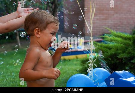 A fun holiday with balls and bubbles. A white boy on the playground in a stream of soap bubbles Stock Photo