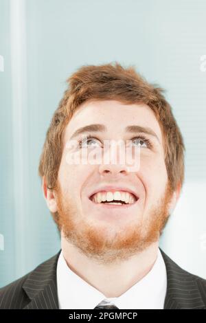 Close-up portrait of young man with short red hair and beard. Joyful and somewhat foolish expression as he looks up smiling or laughing happily, chin Stock Photo