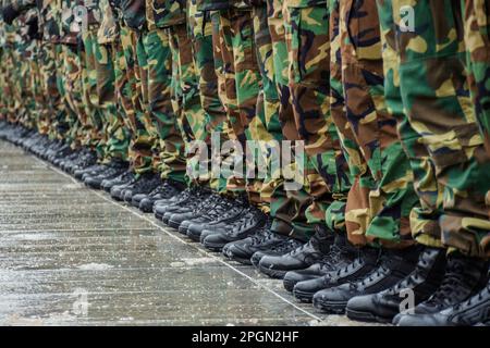 A close-up view of a row of soldiers standing in formation on a wet pavement, wearing black combat boots and camouflage military uniforms Stock Photo