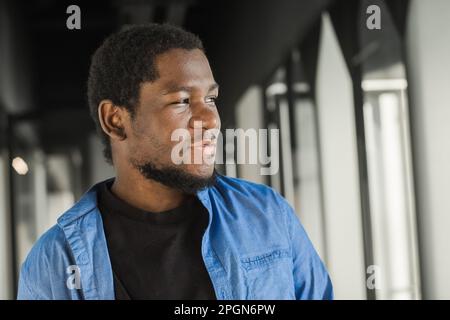 Close-up black serious male face in profile. Man stand with arms folded. Portrait of pensive african american man looking out window in office Stock Photo