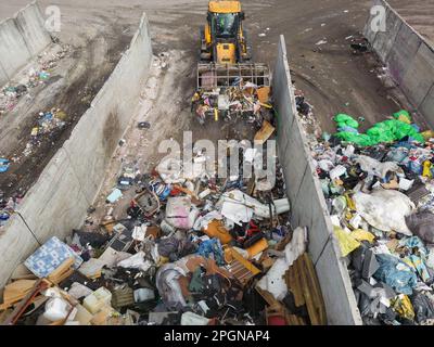 Wheeled loader loading bucket with garbage material and moving it, doing waste management tasks at a landfill, drone view Stock Photo