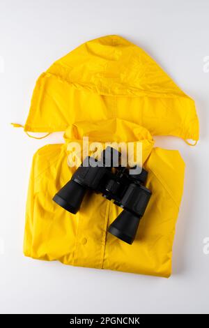 Close up of yellow rainproof coat and binoculars on white background with copy space Stock Photo