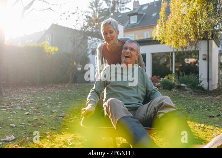 Happy senior couple having fun with wheelbarrow in garden Stock Photo
