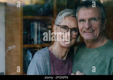 Portrait of happy senior couple behind windowpane Stock Photo