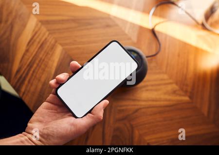 Man connecting phone with blank screen to smart speaker on kitchen counter Stock Photo