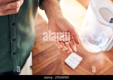 Male hand holding pill, blister pack lying on kitchen counter Stock Photo