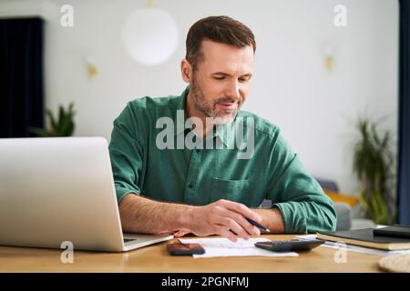 Man at home sitting with laptop and documents examining home finances Stock Photo