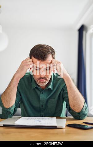 Worried man looking at document with financial figuers while sitting at table at home Stock Photo