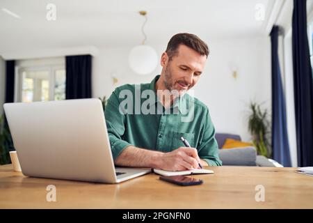 Handsome man working from home taking notes at desk Stock Photo