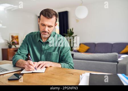 Handsome man working from home taking notes at desk Stock Photo