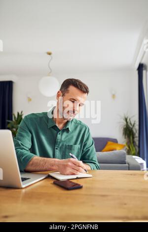 Handsome man working from home taking notes at desk Stock Photo