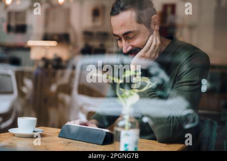 Smiling man watching videos on tablet PC in cafe Stock Photo
