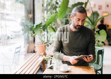 Mature man using tablet PC sitting at table in cafe Stock Photo