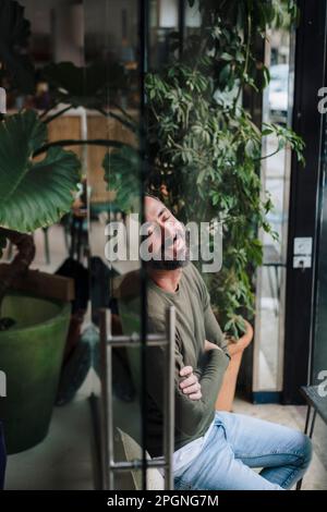 Smiling mature man with arms crossed relaxing in cafe Stock Photo