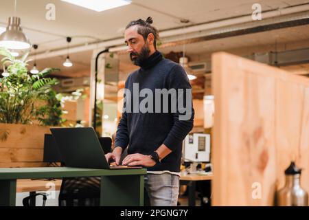 Businessman using laptop standing by desk in office Stock Photo
