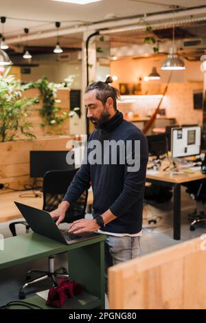 Mature businessman working on laptop standing by desk Stock Photo