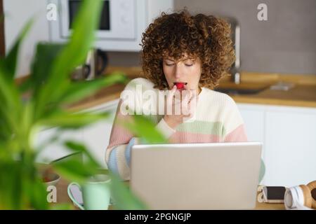 Freelancer eating raspberry and working on laptop at home Stock Photo