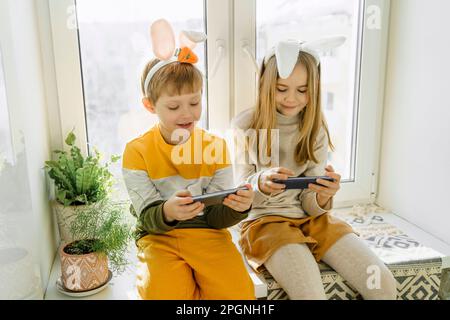Happy girl and boy playing video games on smart phone at home Stock Photo
