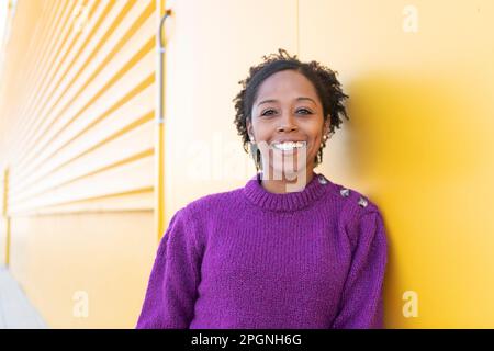 Happy woman wearing sweater standing by yellow wall Stock Photo