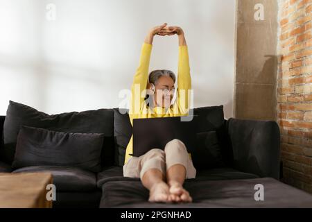 Smiling freelancer stretching arms sitting on sofa at home Stock Photo