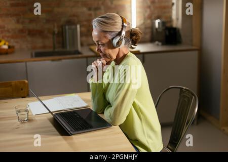 Freelancer wearing wireless headphones using laptop at desk Stock Photo